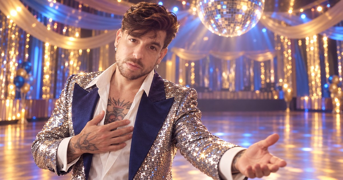 Mike Saint Louis con chaqueta de lentejuelas plateadas y solapas azules, la mano en el pecho, bajo una bola de espejos en una pista de baile iluminada.