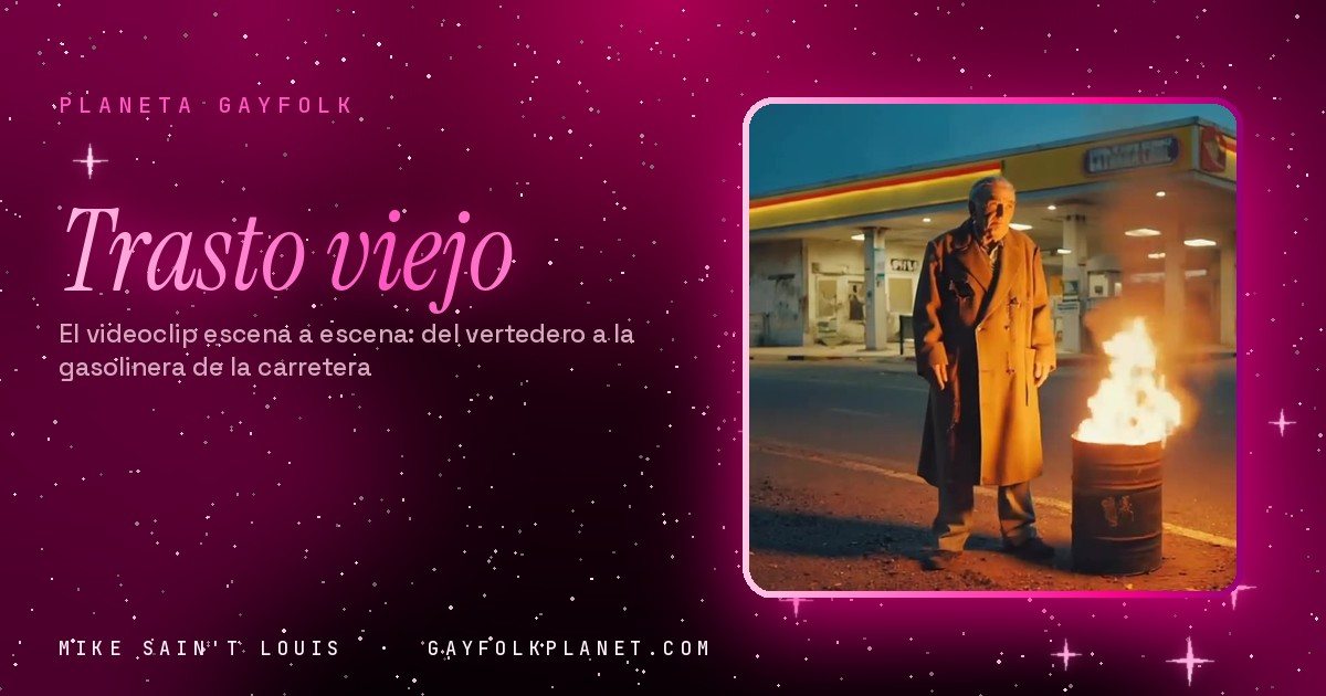 Fotograma de «Trasto viejo»: un anciano con abrigo largo de color camel, de pie junto a un bidón con fuego delante de una gasolinera de carretera al anochecer