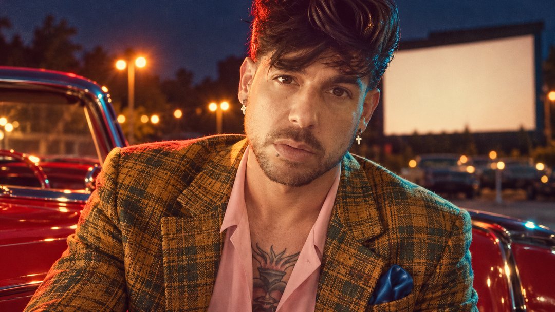 Mike Sain't Louis con americana de cuadros y camisa rosa en un autocine de noche junto a un coche rojo — foto retro PLANETA GAYFOLK.