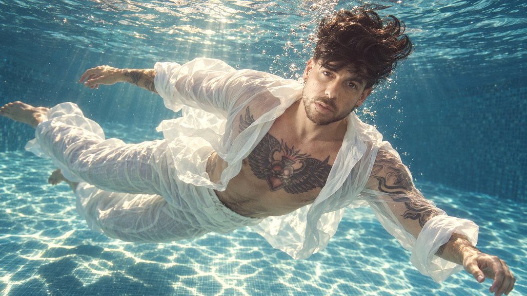 Mike Sain't Louis con camisa y pantalón blancos flotando bajo el agua en una piscina — retrato Tupé Grease PLANETA GAYFOLK.