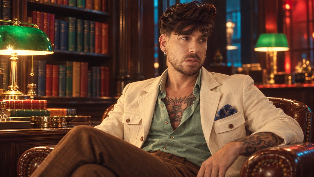 Mike Sain't Louis con americana crema y camisa verde sentado en una biblioteca con lámparas verdes — foto retro PLANETA GAYFOLK.