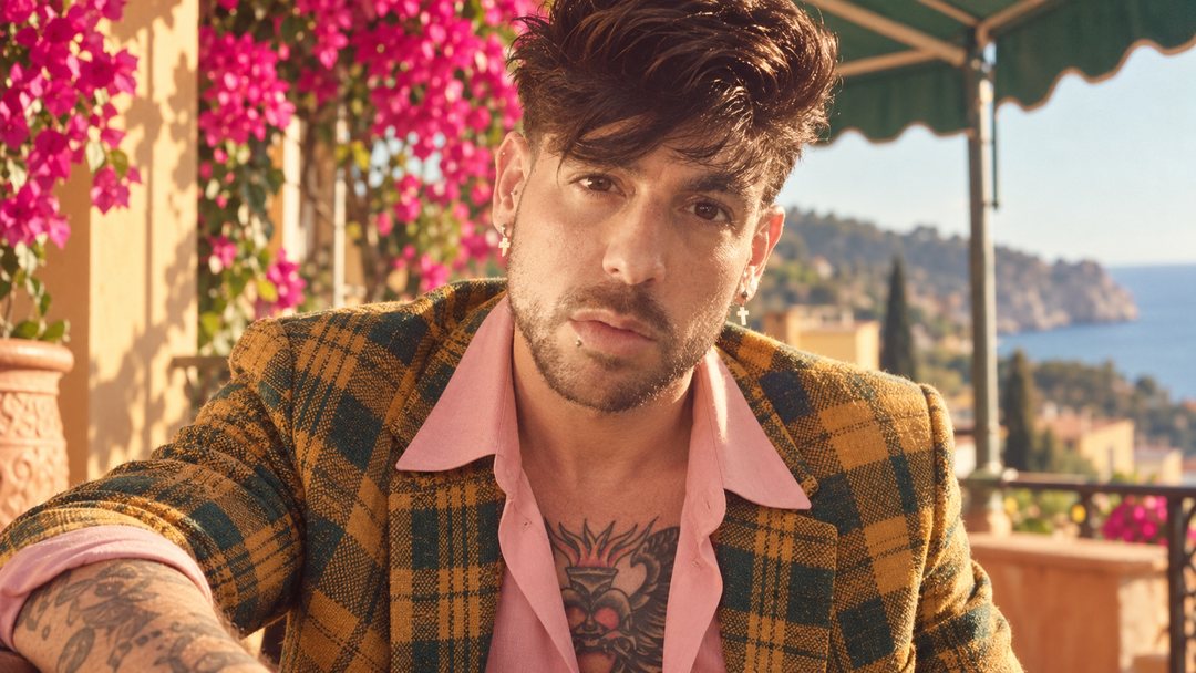 Mike Sain't Louis con americana de cuadros ocre y camisa rosa junto a unas buganvillas sobre el mar — foto retro PLANETA GAYFOLK.