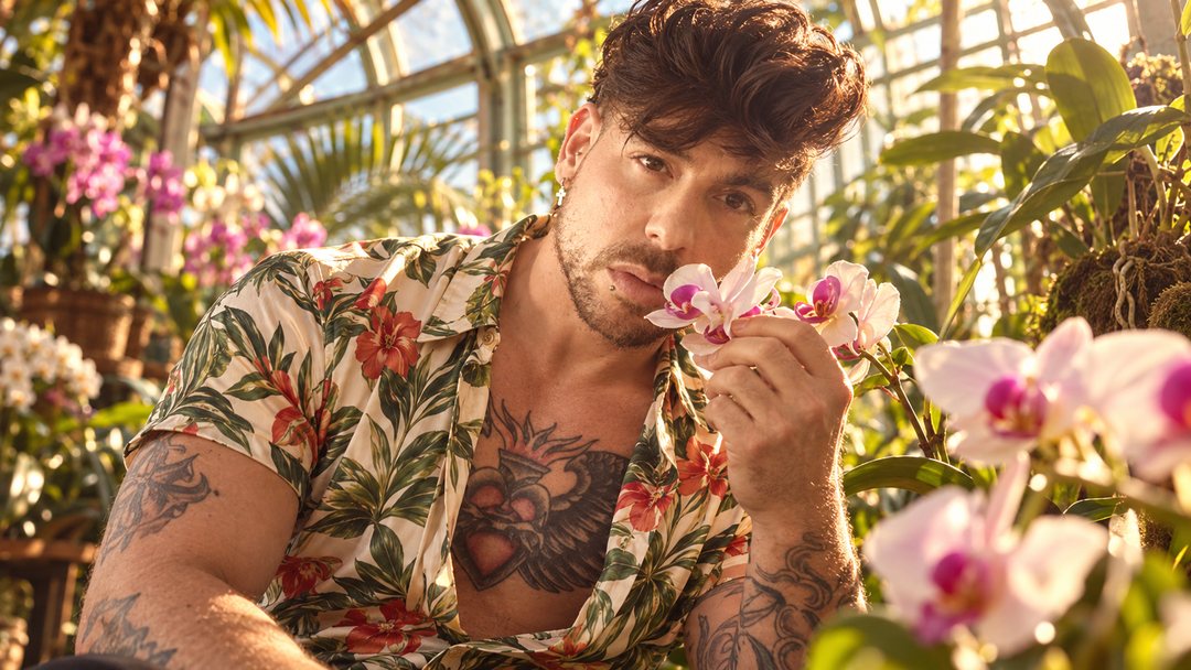 Mike Sain't Louis con camisa de flores oliendo una orquídea en un invernadero — retrato Tupé Grease PLANETA GAYFOLK.