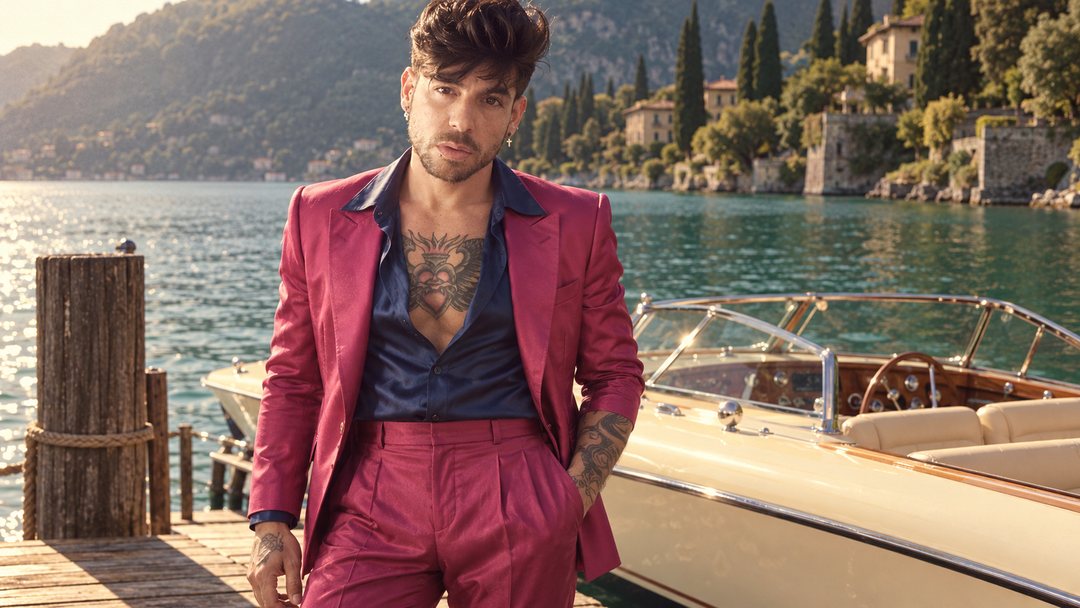 Mike Sain't Louis con traje fucsia junto a una lancha de madera en un lago rodeado de cipreses — foto retro PLANETA GAYFOLK.