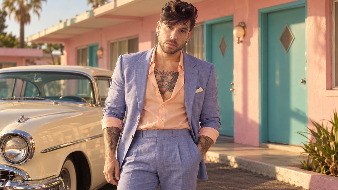 Mike Sain't Louis con traje lavanda junto a un coche clásico ante un motel de paredes rosas y puertas turquesa — foto retro PLANETA GAYFOLK.