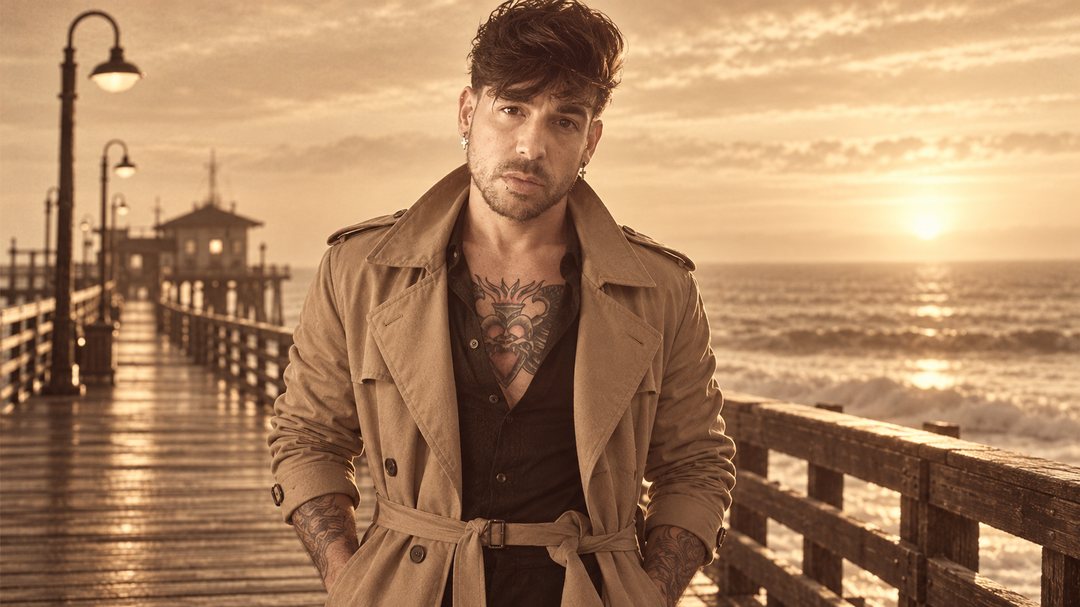 Mike Sain't Louis con gabardina beige en un muelle de madera frente al mar al atardecer — foto retro PLANETA GAYFOLK.