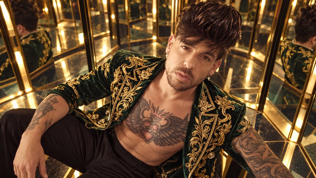 Mike Sain't Louis con chaqueta de terciopelo verde bordada en oro sentado en una sala de espejos dorados — retrato Tupé Grease PLANETA GAYFOLK.