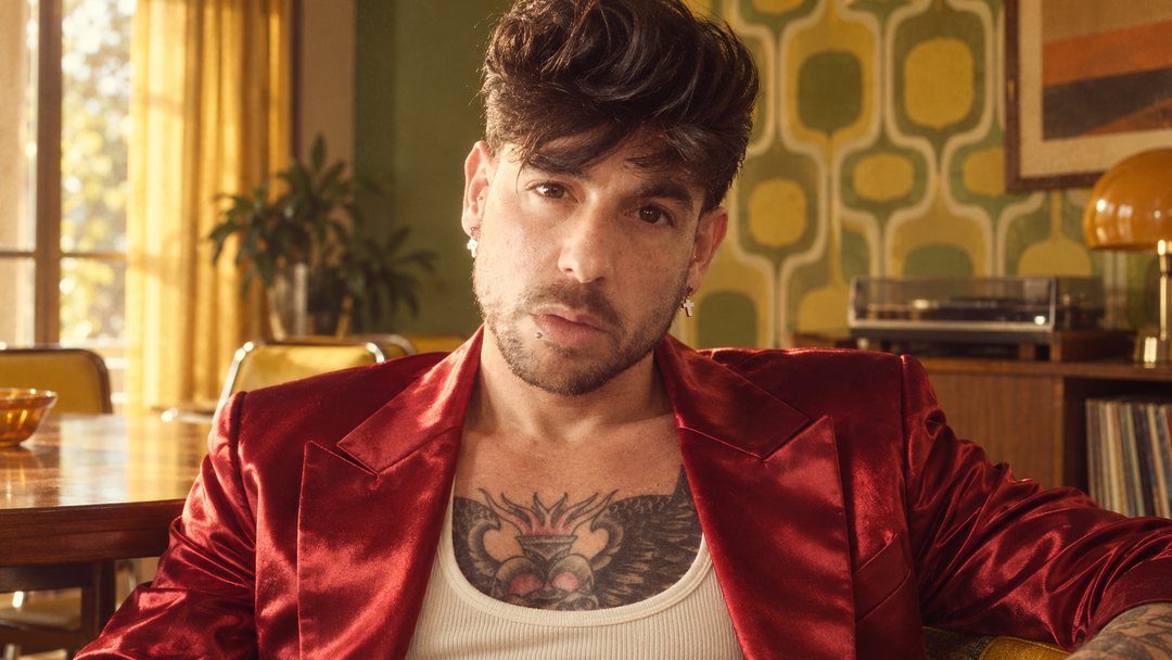 Mike Sain't Louis con chaqueta satinada roja y camiseta blanca en un salón con papel pintado geométrico — foto retro PLANETA GAYFOLK.