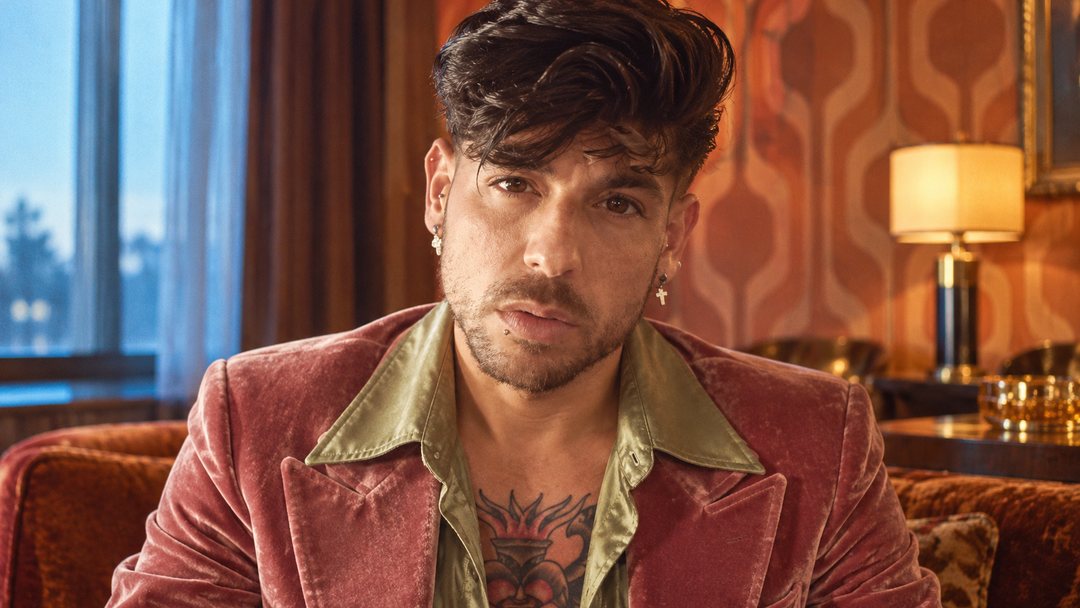 Mike Sain't Louis con chaqueta de terciopelo rosa empolvado y camisa verde en un salón con lámpara y papel pintado — foto retro PLANETA GAYFOLK.