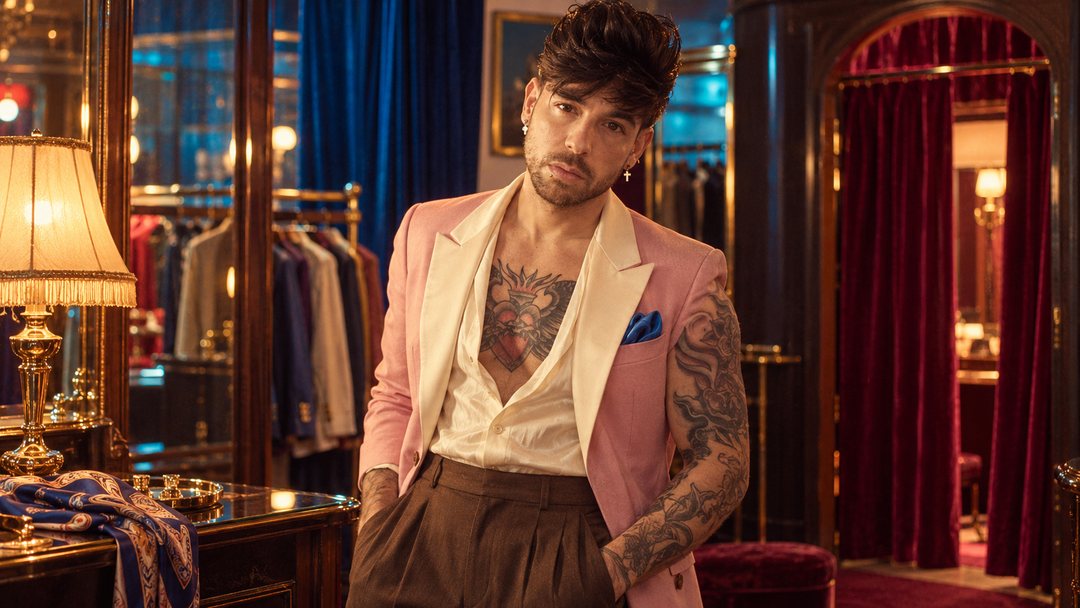 Mike Sain't Louis con americana rosa en una sastrería de noche con perchas y cortinas rojas — foto retro PLANETA GAYFOLK.