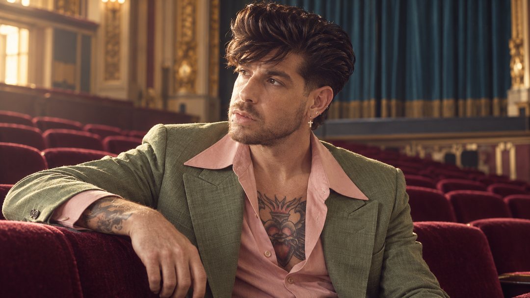 Mike Sain't Louis con americana verde y camisa rosa recostado en las butacas de terciopelo rojo de un teatro — foto retro PLANETA GAYFOLK.