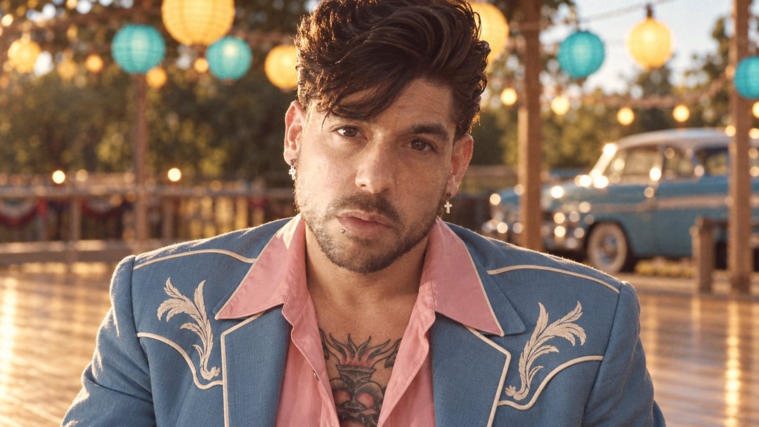 Mike Sain't Louis con chaqueta vaquera bordada de estilo western y camisa rosa en una terraza con farolillos — foto retro PLANETA GAYFOLK.