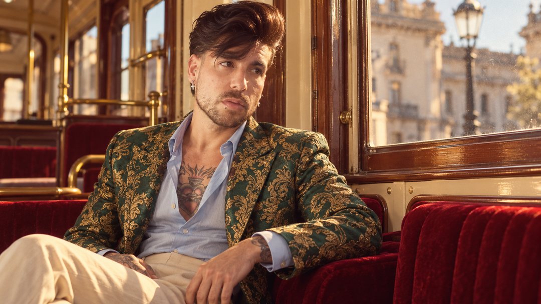 Mike Sain't Louis con chaqueta de brocado verde y dorado sentado en un vagón con asientos de terciopelo rojo — foto retro PLANETA GAYFOLK.